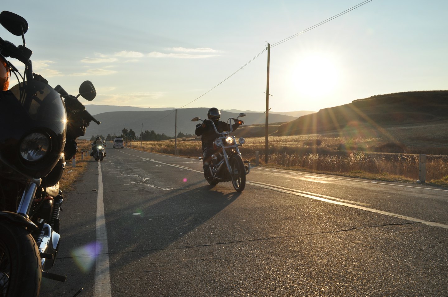 Motorcyclists ride on an asphalt road at sunset.